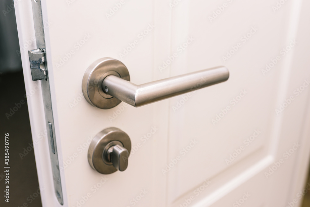 Open the white door. Modern chrome handle in your hotel room or home. Entrance to an apartment, office, or bedroom. Door detail. Interior of a house or hotel. Open the white door. Modern chrome handle in your hotel room or home. Entrance to an apartment, office, or bedroom. Door detail. Interior of a house or hotel.