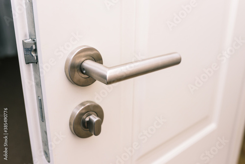 Open the white door. Modern chrome handle in your hotel room or home. Entrance to an apartment, office, or bedroom. Door detail. Interior of a house or hotel.