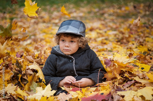 cute curly-haired boy sitting in yellow maple leaves in autumn in the Park