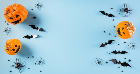 Halloween decorations made from pumpkin, paper bats and black spider on pastel blue background. Flat lay, top view with copy space for text.