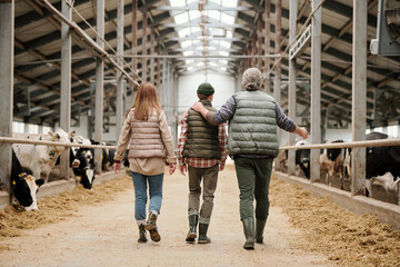 Rear view of father pointing at cows and sharing farm experience with son