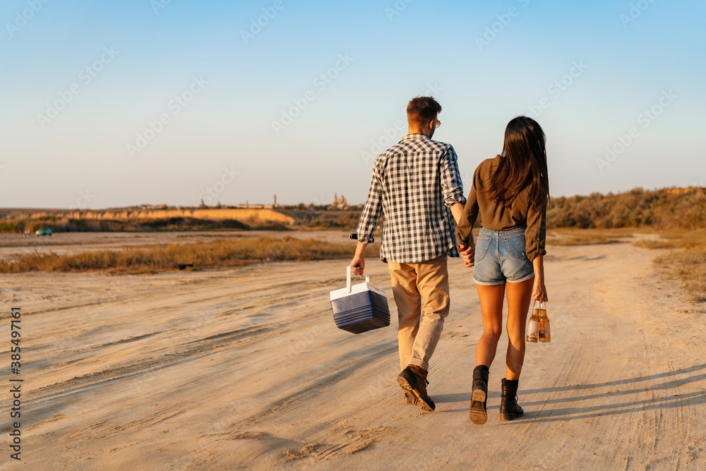 Couple holding hands together while strolling with bear and cooler bag