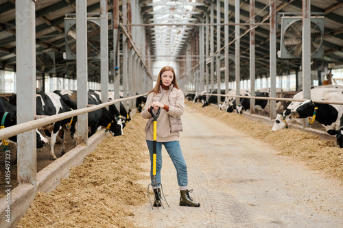 Portrait of serious confident farm woman standing with pitchfork in contemporary cowshed