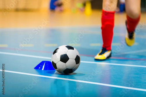Football futsal ball, wooden floor, training marker and running player in cleats. Indoor soccer sports hall. Sport Futsal background. Indoor Soccer Winter League