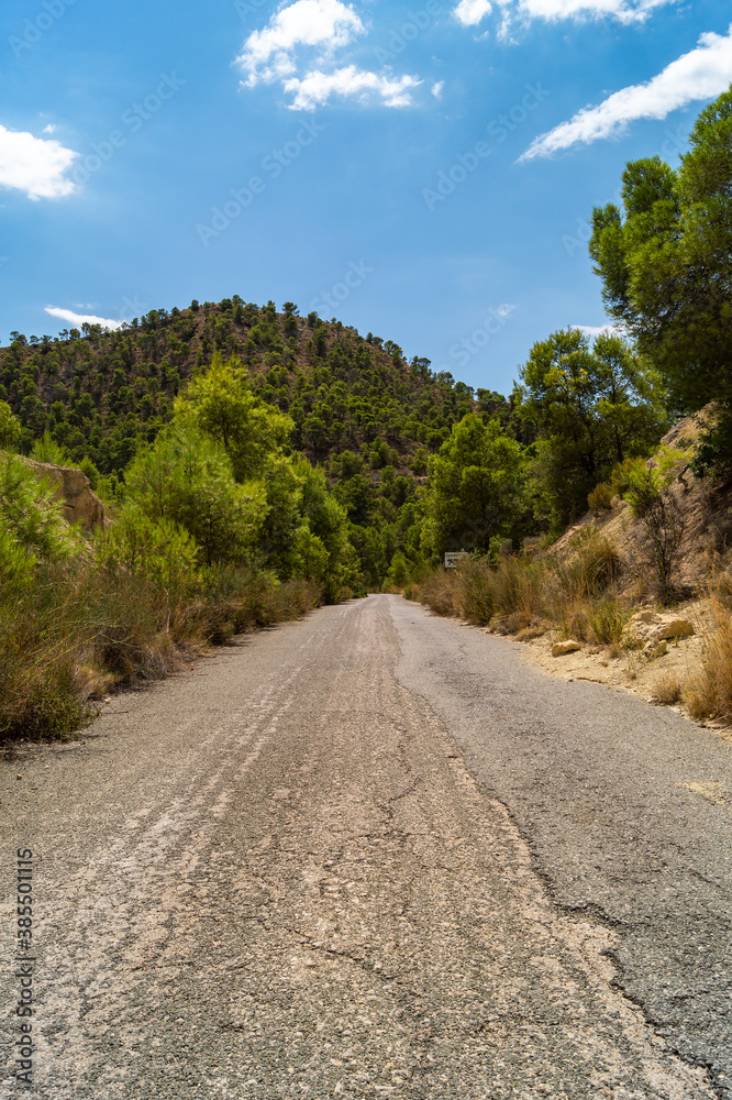 Carretera asfalta en medio de la montaña que conduce al embalse Amadorio en Villajoyosa (Alicante, España). Preciosas vistas en un día soleado con nubes blancas y naturaleza verde que transmite calma.