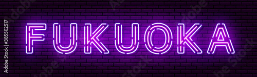 Glowing neon sign with the inscription of the Japan city of Fukuoka. In blue and purple colors. Against a brick wall.
