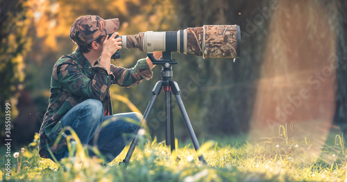 wildlife photographer using telephoto lens with camouflage coating photographing wild life using gimbal head on tripod. professional photography equipment for cinematic shooting in the nature outdoor