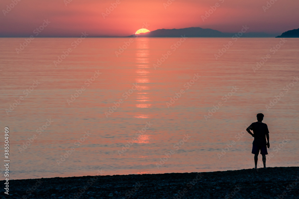 Man looking at the sunset on a mediterranean beach.