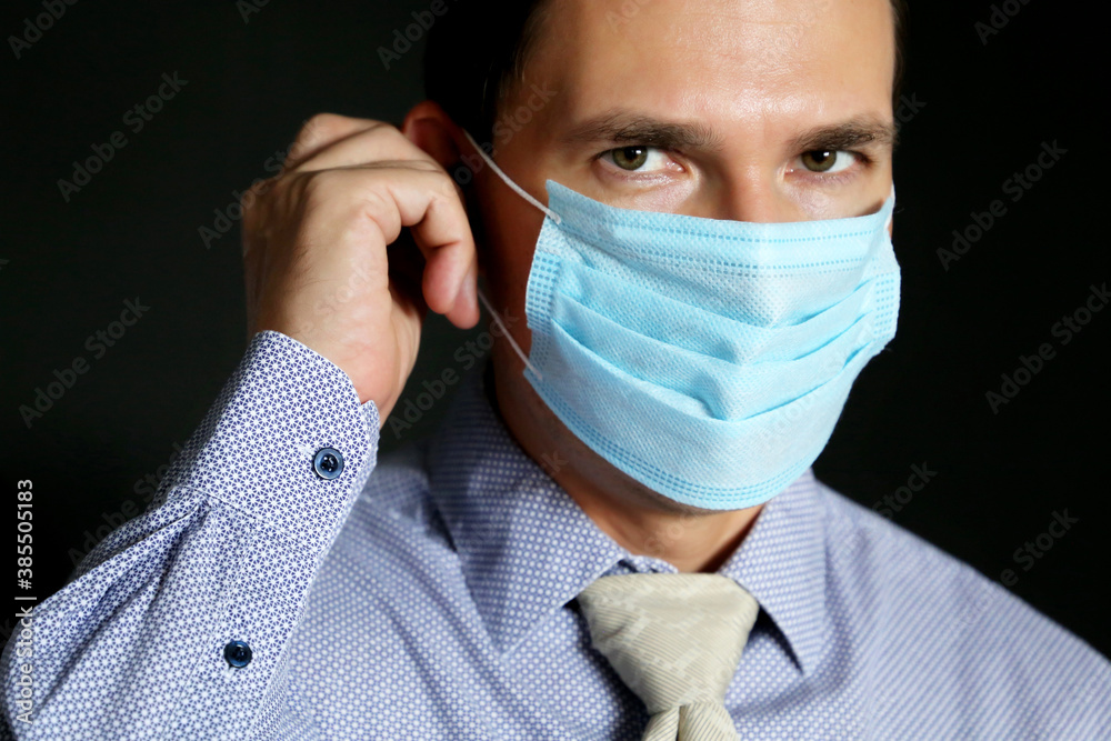 Man in disposable face mask and office clothes on black background. Safety at work during coronavirus pandemic Man in disposable face mask and office clothes on black background. Safety at work during coronavirus pandemic