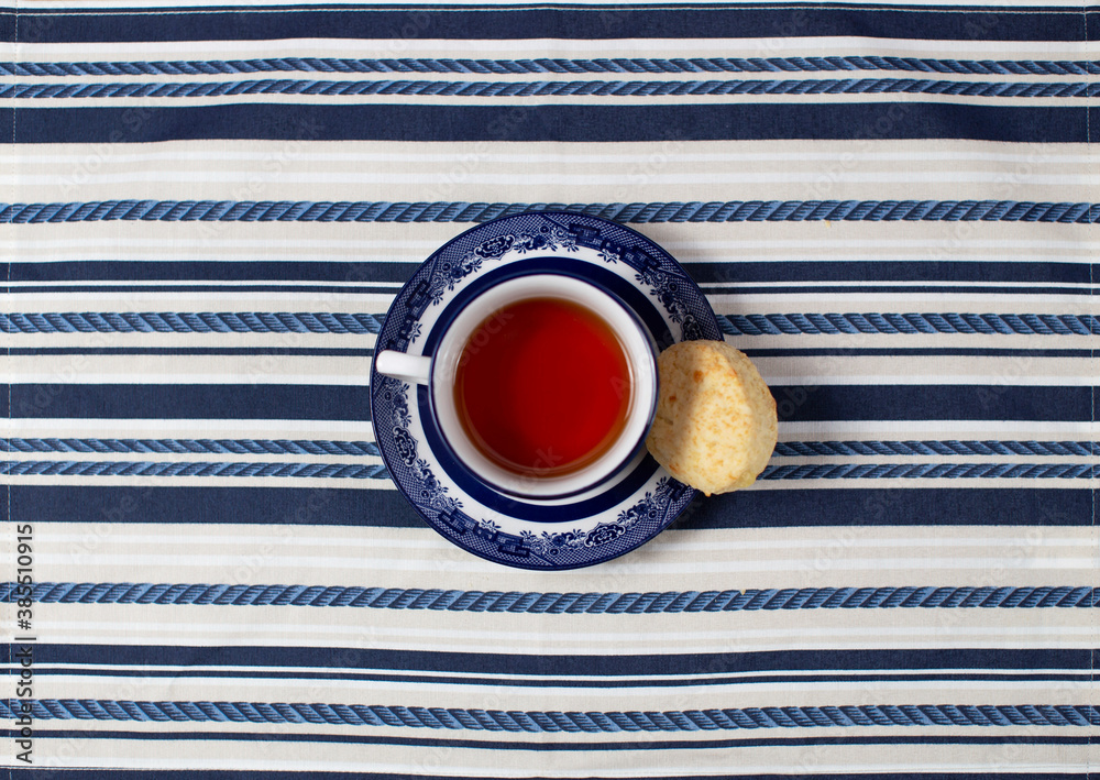 A cup of tea with a cookie in the center on a striped tablecloth; cenital plane - obrazy, fototapety, plakaty 