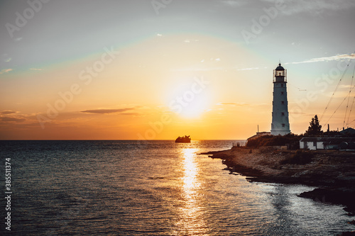 old lighthouse at sunset. a sunken ship in the distance. vertical photo © John