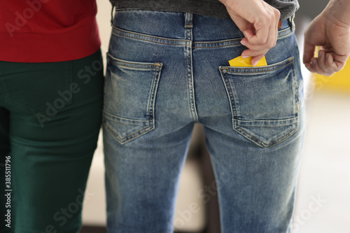 Woman take yellow condom out of pocket, back view. Contraceptives in male back pocket of jeans.