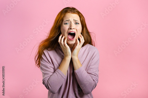 Frightened and screaming woman shocked isolated over pink background. Stressed and depressed pretty girl because of bad news.