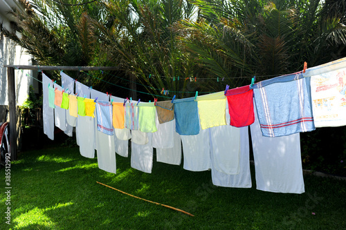 Toallas blancas y trapos de cocina de colores secándose al sol en un tendedero al aire libre photo