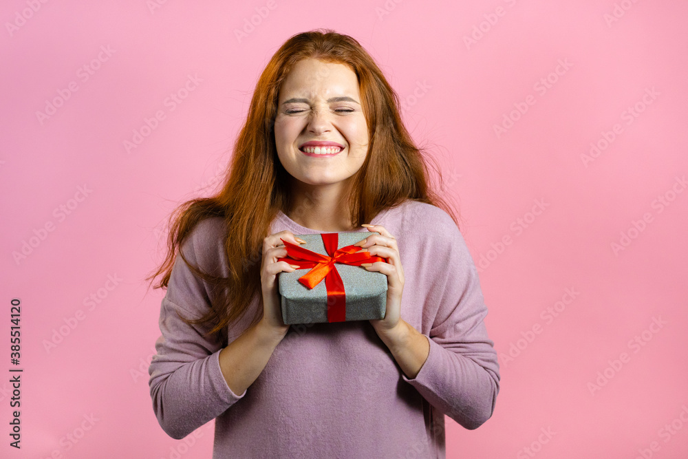 Excited woman received gift box with bow. She is happy and flattered by attention. Girl smiling with present on pink background. Studio portrait Excited woman received gift box with bow. She is happy and flattered by attention. Girl smiling with present on pink background. Studio portrait