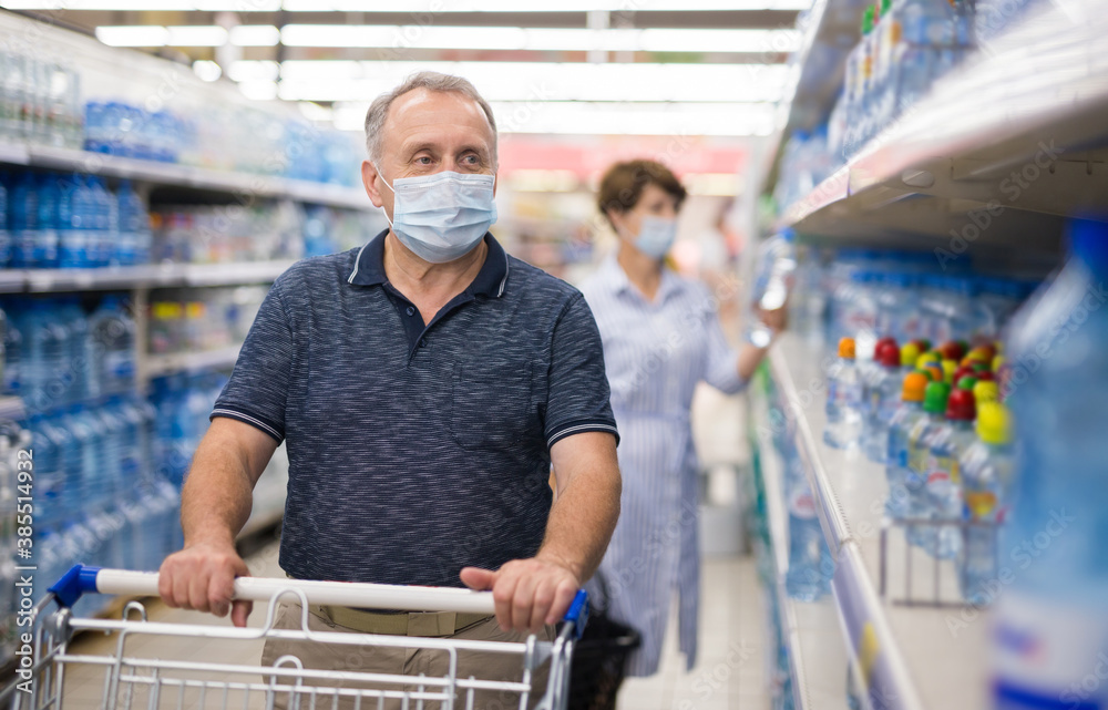 Man in protective mask picks water bottles on supermarket