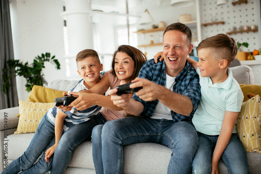 Husband and wife playing video games with joysticks in living room. Loving couple are playing video games with kids at home