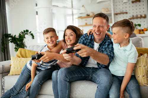 Husband and wife playing video games with joysticks in living room. Loving couple are playing video games with kids at home