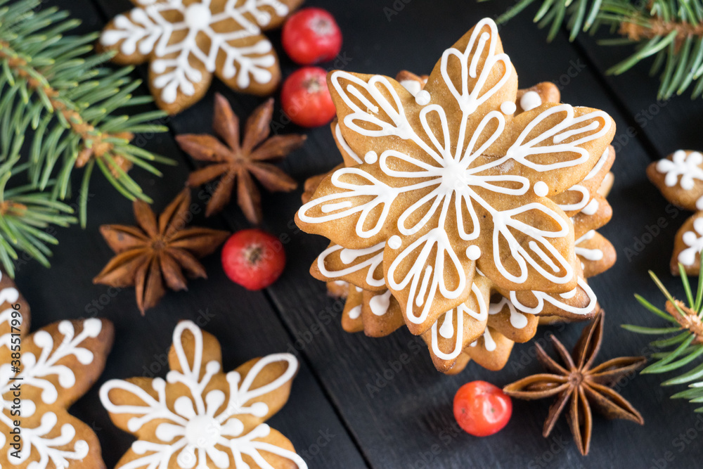 Gingerbread cookies snowflakes decorated with icing with fir-tree branches and berries on black wooden background. Close-up, selective focus