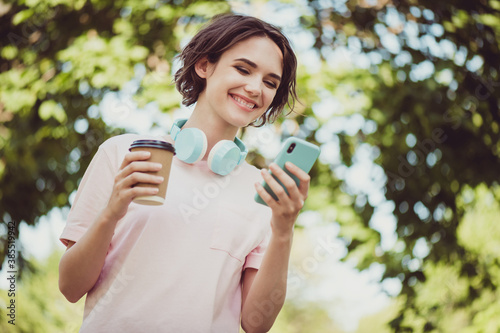 Photo of charming lovely cute lady cheerful look hands hold telephone cup coffee typing chatting friend setting out forest night trip together wear headphones white shirt outside