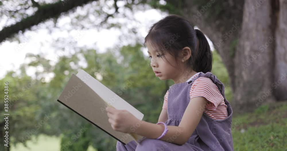 A pretty little Asian girl reading a book under the big tree. A pretty little Asian girl reading a book under the big tree.