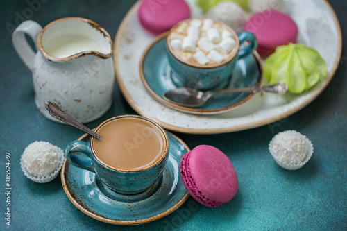 Blue coffee cups with cream and marshmallows, with coconut candies on a blue background