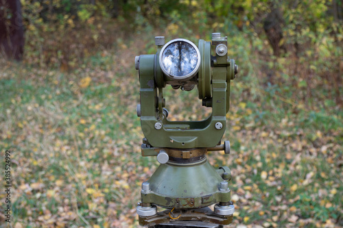 Old optical theodolite for geodetic works on the background of the forest.