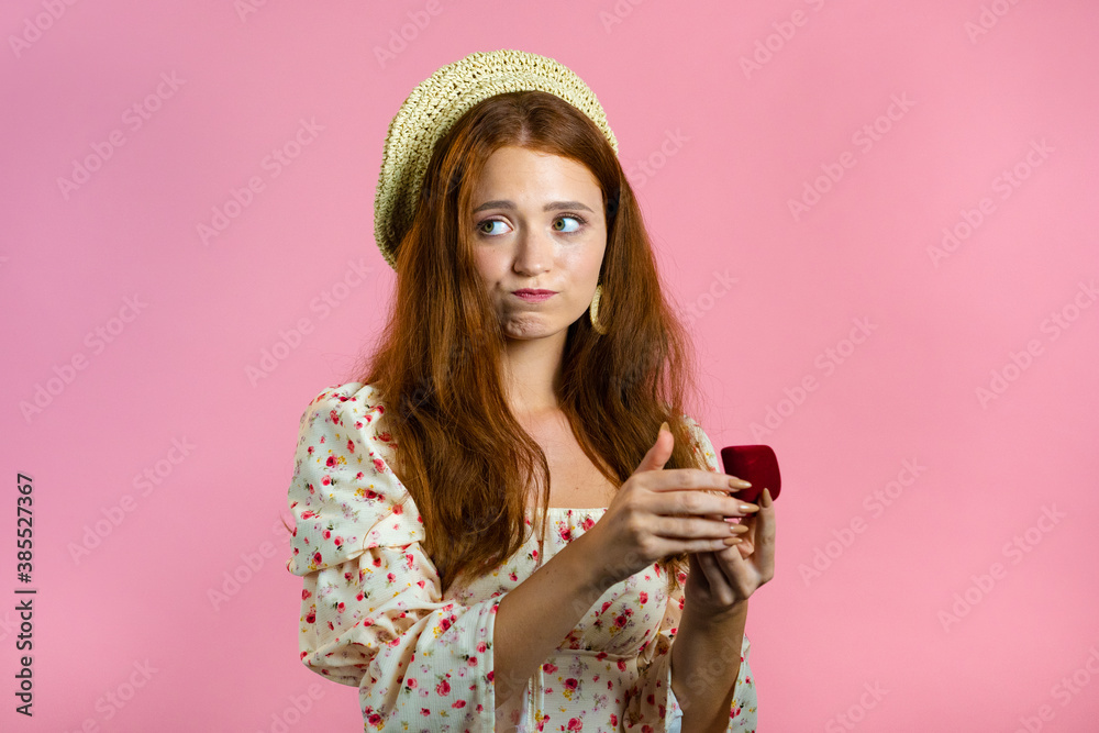 Disappointed upset girl, she doesn't like gift. Pretty european woman in floral dress holding small jewelry box with marriage proposal on pink background. Disappointed upset girl, she doesn't like gift. Pretty european woman in floral dress holding small jewelry box with marriage proposal on pink background.