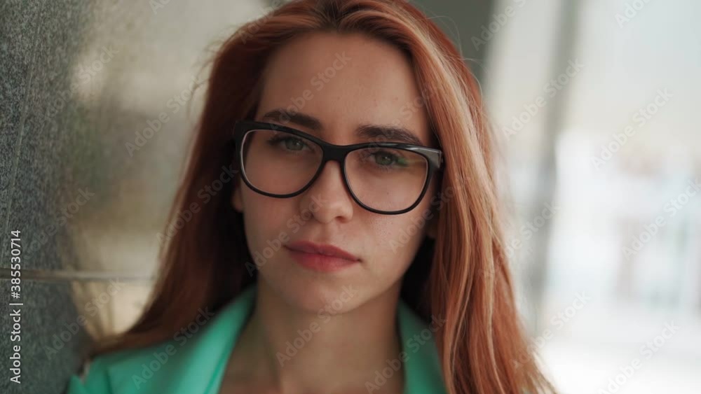 Portrait of a beautiful young woman in glasses with long red hair looks into the camera. Pretty lady close-up. Slow motion Portrait of a beautiful young woman in glasses with long red hair looks into the camera. Pretty lady close-up. Slow motion