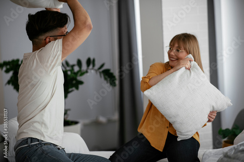 Boyfriend and girlfriend fighting pillows on the bed. Happy couple having fun at home..