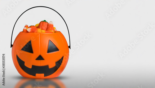 Halloween pumpkin Jack-o-lantern bucket with candy corn for celebration halloween. Orange pumpkin with scary smile face Jack-o-lantern. Bucket for candy. Trick or treat and Happy Halloween