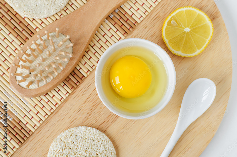 Raw egg in the small white bowl, lemon slice and wooden hair brush. Natural homemade hair treatment and zero waste concept. Top view, copy space Raw egg in the small white bowl, lemon slice and wooden hair brush. Natural homemade hair treatment and zero waste concept. Top view, copy space