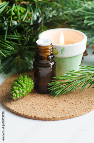 Small glass bottle with essential pine oil  pine branches  green cone and burning candle. Aromatherapy  spa and herbal medicine ingredients. Copy space.