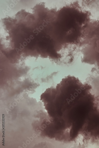 portrait image of a group of storm clouds, shaded in brown, surrounding a cloudy sky.