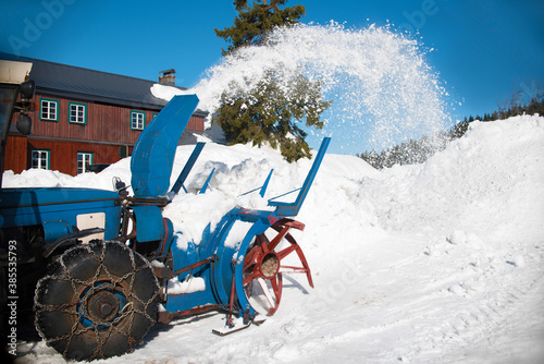 Rustic rotary snow blower blows blurred snow to clear road. Old machinery prepares new parking lots for tourists and Jizerska 50 km cross country skiers in Jizerka settlement, Jizerske hory mountains photo