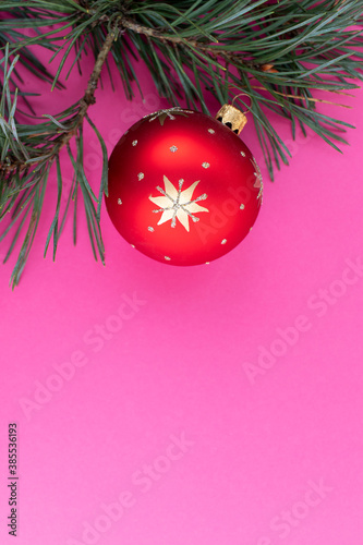 Christmas tree branch with red decoration on pink background. Top view, flat lay.