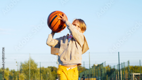 Happy little boy playing basketball outdoors