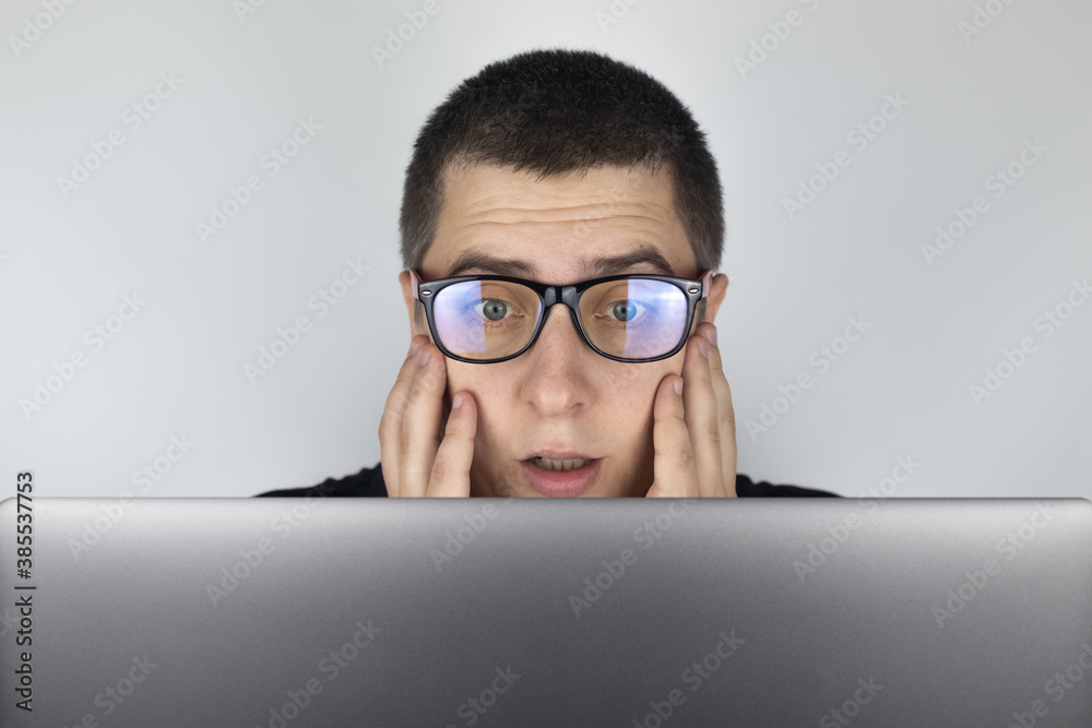 The man looks at the laptop and is frightened by what he saw there. Expressing emotions and reacting to what you see on the Internet. Shocking content concept. The man looks at the laptop and is frightened by what he saw there. Expressing emotions and reacting to what you see on the Internet. Shocking content concept.
