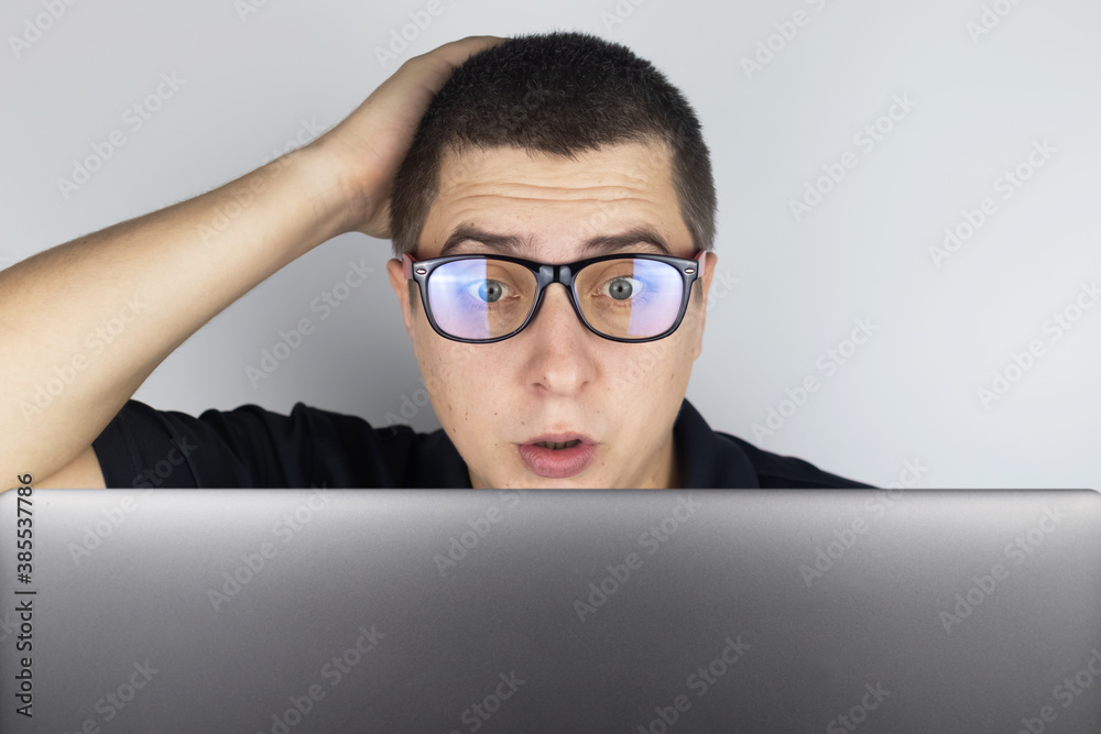 The man looks at the laptop and is frightened by what he saw there. Expressing emotions and reacting to what you see on the Internet. Shocking content concept. The man looks at the laptop and is frightened by what he saw there. Expressing emotions and reacting to what you see on the Internet. Shocking content concept.