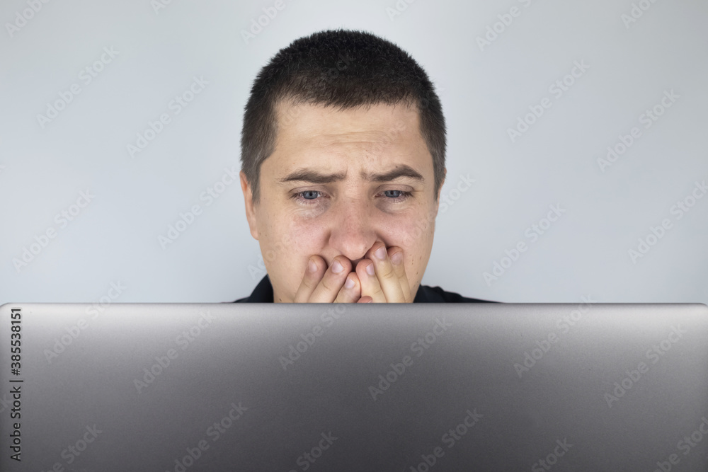 The man looks at the laptop, is embarrassed and ashamed of what he saw there. Expressing emotions and reacting to what you see on the Internet. Shocking content concept. The man looks at the laptop, is embarrassed and ashamed of what he saw there. Expressing emotions and reacting to what you see on the Internet. Shocking content concept.