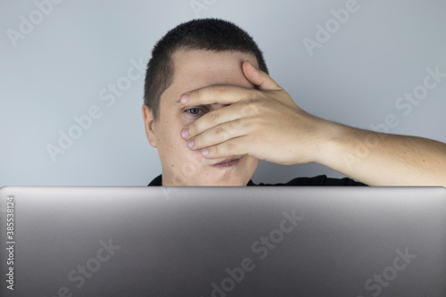 The man looks at the laptop, is embarrassed and ashamed of what he saw there. Expressing emotions and reacting to what you see on the Internet. Shocking content concept.