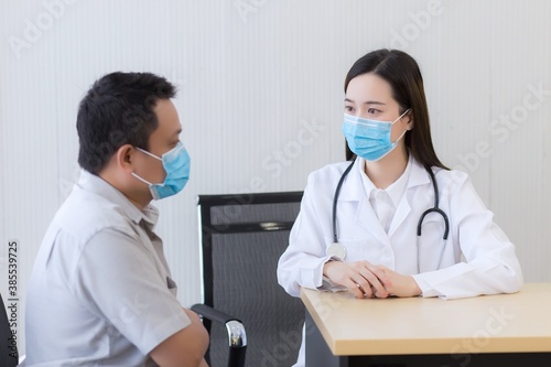 Asian woman doctor talking with a man patient about his pain and symptom while they put on a face mask to prevent Coronavirus disease in hospital.