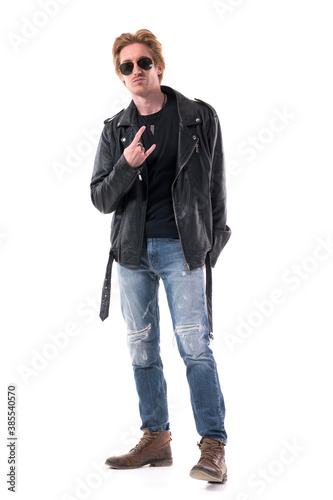 Macho rocker man showing two finger horns or devil hand sign gesture in black leather jacket. Full body isolated on white background. © sharplaninac