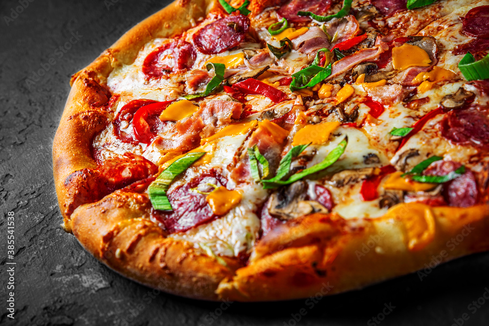 Pizza with Mozzarella cheese, salami, chicken meat, beef, ham, Tomato sauce, pepper, spices. Italian pizza on Dark grey black slate background