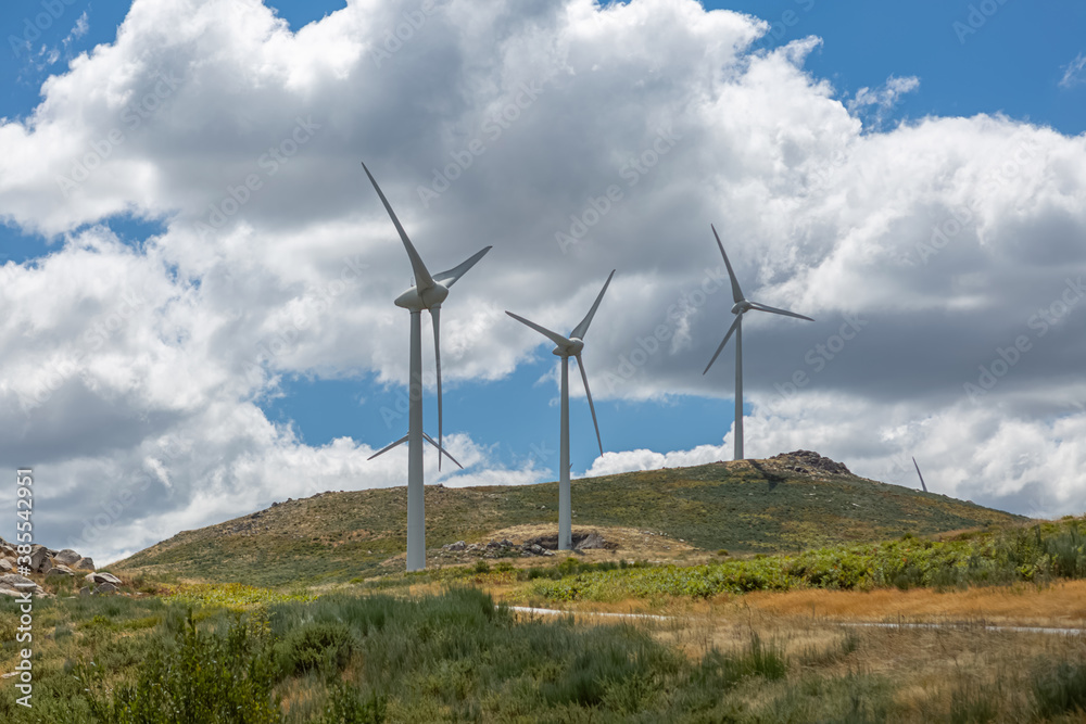 View of a wind turbines on top of mountains, cloudy sky as background