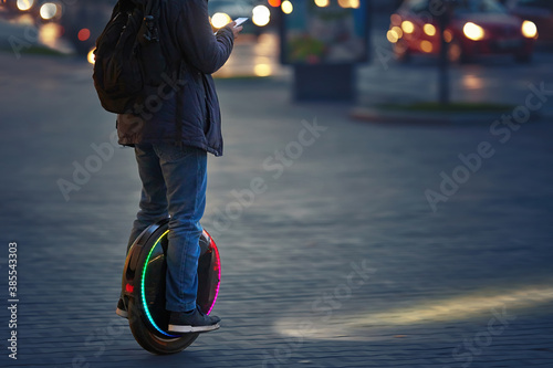 Man riding fast on electric unicycle on city street at night with diode headlights. Mobile portable individual transportation vehicle. Night riding, man on electric mono-wheel riding fast (EUC) photo