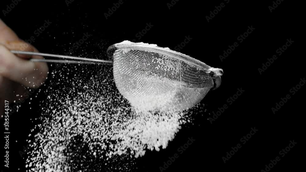 Flour sifting with sieve for pie and cupcake making. Chef confectioner sifts powdered sugar or flour in sieve slow motion isolated on black background. cooking desserts with sugar powder.