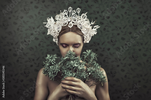 Beautiful young blonde woman with a traditional tembleque headdress, holding flowers towards her face, in front of a grey flower pattern wallpaper photo