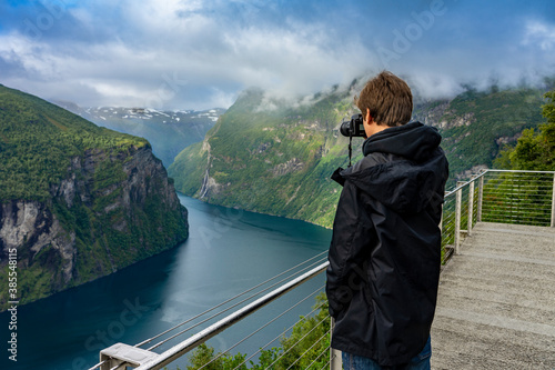 Urlaub in Süd-Norwegen: der epische Geiranger Fjord - junger Mann / Jugendlicher fotografiert vom Aussichtspunkt den Fjord (Ørnesvingen) photo