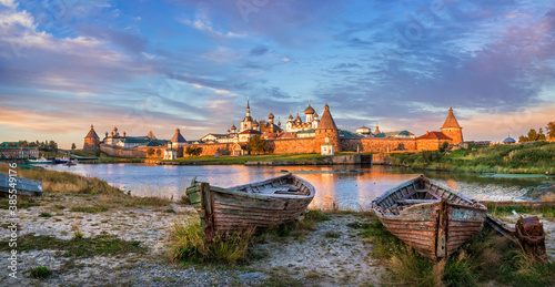 Old wooden boats on the shore and a view of the temples of the Solovetsky Monastery